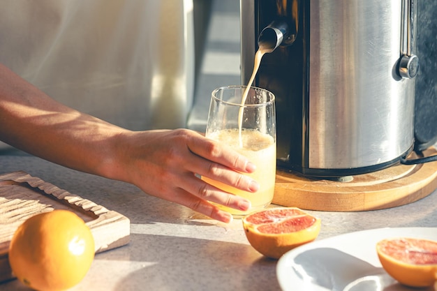 Eine Frau macht zu Hause in der Küche Orangensaft mit einer elektrischen Saftpresse