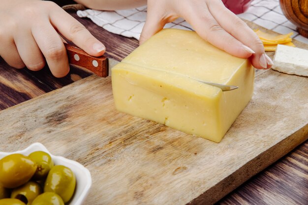Eine Frau schneidet holländischen Käse auf einer Holzbrett-Seitenansicht