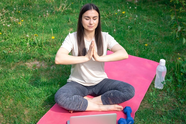 Kostenloses Foto eine frau sitzt vor einem laptop auf einem teppich im park und meditiert