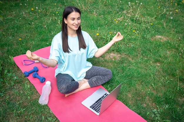 Kostenloses Foto eine frau sitzt vor einem laptop auf einem teppich im park und meditiert