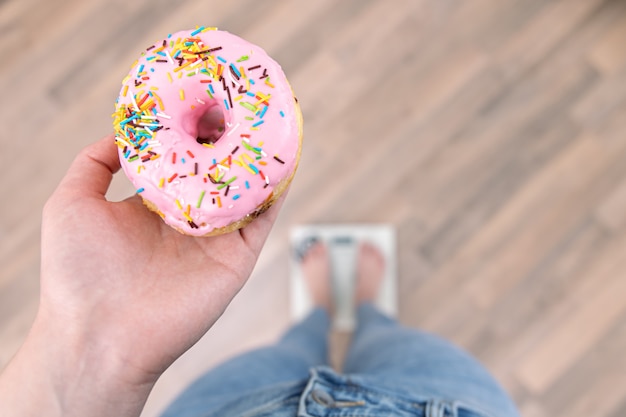 Eine Frau steht auf der Waage, hält einen Donut in den Händen, das Konzept der Ernährung, Gewichtszunahme, Gewichtsverlust, richtige Ernährung, süß.
