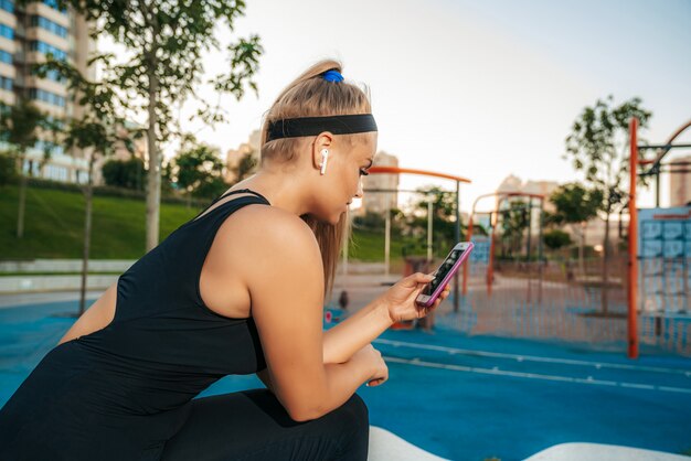 Eine Frau steht mit einem Telefon im Fitnessstudio im Freien