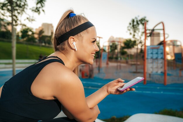 Eine Frau steht mit einem Telefon im Fitnessstudio im Freien