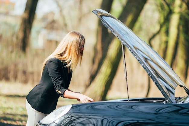 Eine Frau wartet in der Nähe ihres am Straßenrand kaputten Autos auf Hilfe.