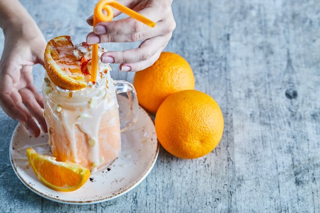 Eine Frauenhand, die einen weißen Teller mit Orangen-Smoothie und Orangenscheibe hält