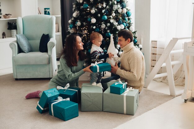 Eine fröhliche Familie mit einem kleinen Kind, das zusammen Spaß nahe dem Weihnachtsbaum hat