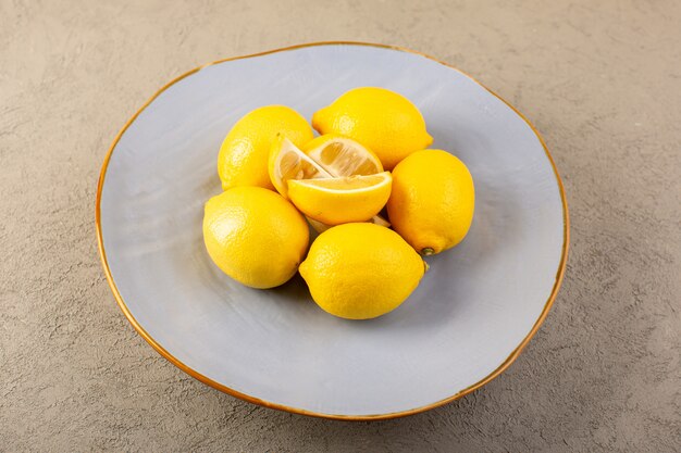 Eine gelbe frische Zitronen der Draufsicht milde und saftige ganze und geschnittene innere blaue Platte auf dem grauen Hintergrund trägt Zitrusfarbe