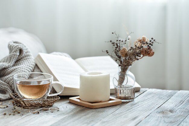 Eine gemütliche Komposition mit einer Tasse Tee, einem Buch und Dekordetails im Inneren des Raumes auf unscharfem Hintergrund.