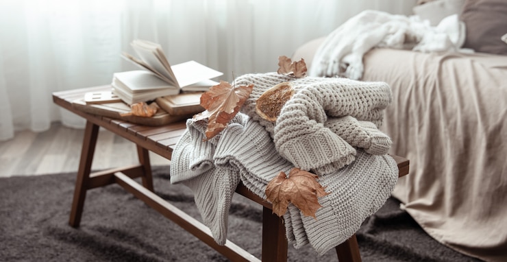 Kostenlose Foto eine gemütliche wohnkomposition mit einem strickpullover, einem buch und blättern im inneren des raumes.