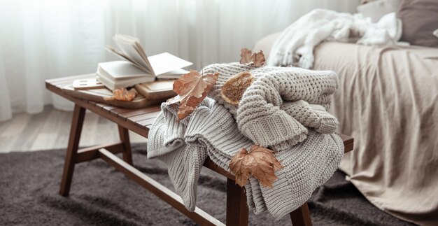 Eine gemütliche Wohnkomposition mit einem Strickpullover, einem Buch und Blättern im Inneren des Raumes.