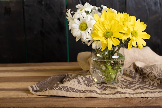 Eine Glasvase mit gelben und weißen Blumen