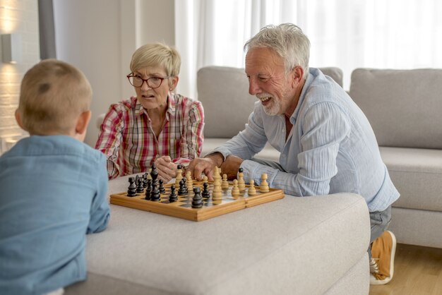 Eine Großmutter und ein Großvater spielen Schach mit einem lächelnden Enkel