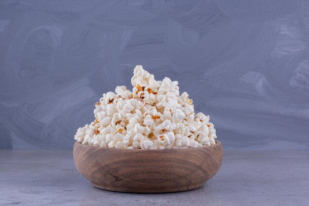 Eine großzügige Portion frisch gekochtes Popcorn in einer Holzschale auf Marmorhintergrund. Foto in hoher Qualität