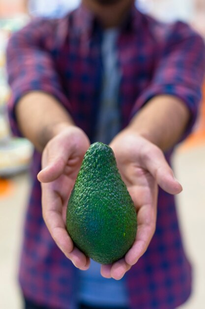 Eine grüne Avocado in den Händen eines Verkäufers