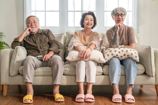 Eine Gruppe asiatischer älterer Männer und Frauen, die am Wochenende zusammen Zeit verbringen, sitzen auf der Couch und schauen sich eine Fernsehkomödie mit fröhlichem Lachen, lächelndem Glücksausdruck an, Senioren im Pflegeheim