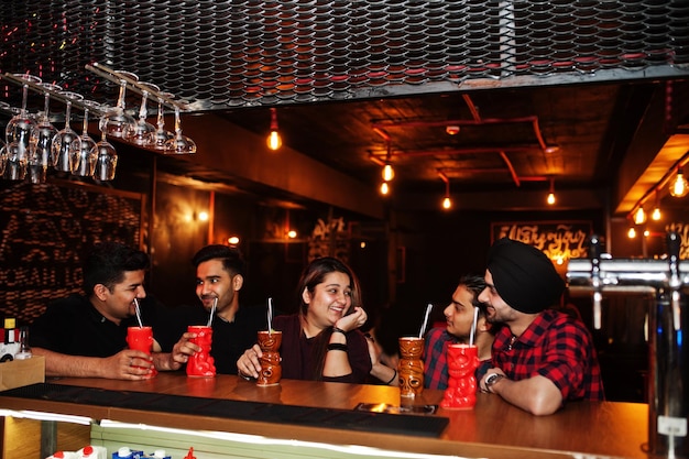 Eine Gruppe indischer Freunde, die Spaß haben und sich im Nachtclub ausruhen und Cocktails in der Nähe der Bartheke trinken