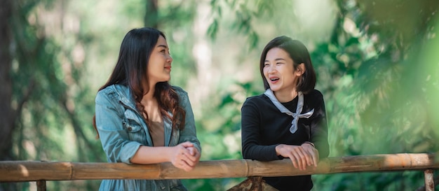 Eine Gruppe junger asiatischer Frauen, die auf einer Bambusbrücke stehen, schauen beim Camping im Wald mit Glück zusammen auf die schöne Natur