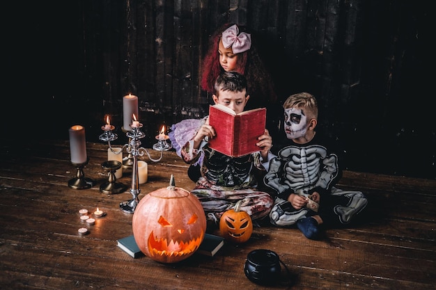 Eine Gruppe süßer gemischtrassiger Kinder in gruseligen Kostümen, die während der Halloween-Party in einem alten Haus Horrorgeschichten lesen. Halloween-Konzept.