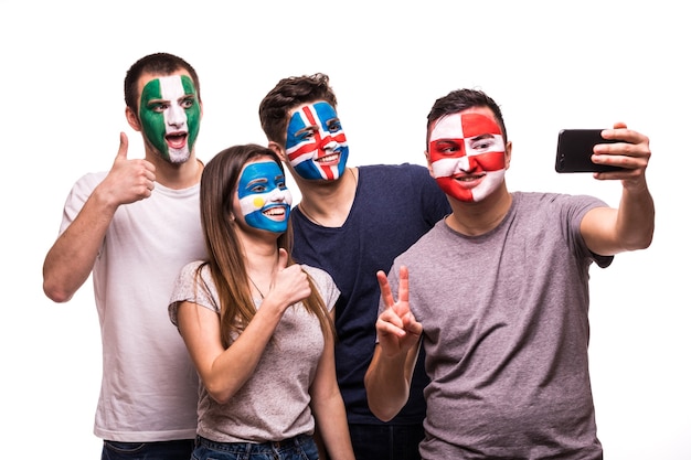 Eine Gruppe von Fans unterstützt ihre Nationalmannschaften mit bemalten Gesichtern. Argentinien, Kroatien, Island, Nigeria Fans nehmen Selfie am Telefon isoliert auf weißem Hintergrund