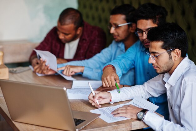 Eine Gruppe von vier südasiatischen Männern posierte bei einem Geschäftstreffen im Café Indianer zusammen und unterzeichnete wichtige Dokumente Vertrag zum Studieren und Arbeiten