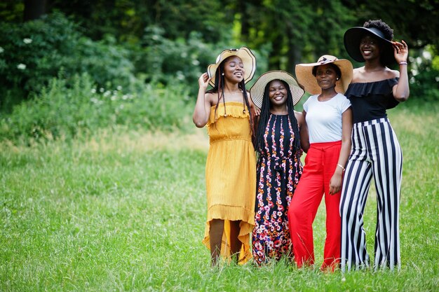 Eine Gruppe von vier wunderschönen afroamerikanischen Frauen trägt einen Sommerhut, der Zeit auf grünem Gras im Park verbringt