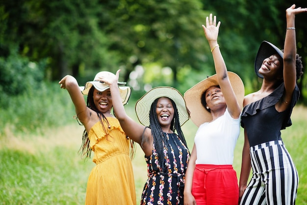 Eine Gruppe von vier wunderschönen afroamerikanischen Frauen trägt einen Sommerhut, der Zeit auf grünem Gras im Park verbringt