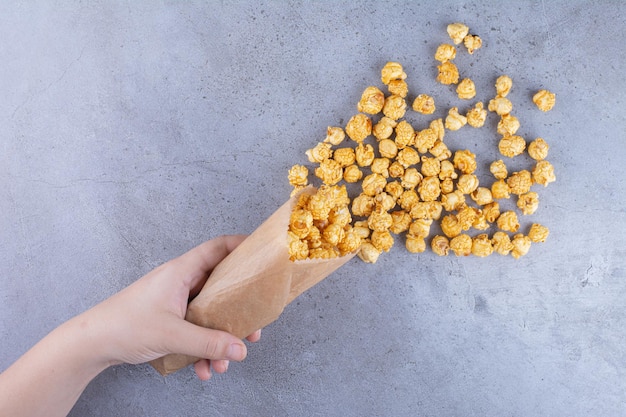 Eine hand, die eine packung mit karamell überzogenes popcorn auf marmoroberfläche verschüttet