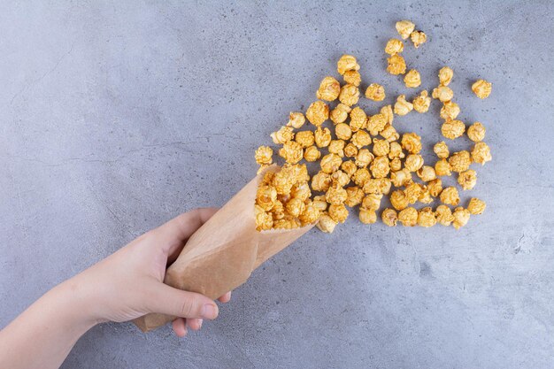 Eine Hand, die eine Packung mit Karamell überzogenes Popcorn auf Marmoroberfläche verschüttet