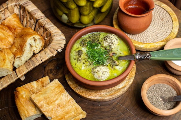 Eine heiße Suppe der oberen Nahaufnahmeansicht innerhalb des braunen runden Topfes zusammen mit geschnittenem gesalzenem Gurkenbrot und Gewürzen