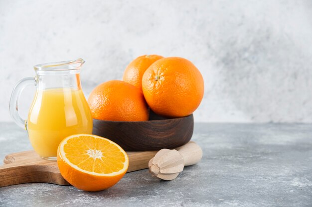 Eine Holzschale mit frischen Orangenfrüchten und ein Glas Krug Saft.