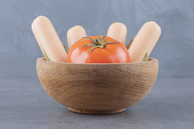 Eine Holzschale mit gekochten Würstchen mit roten Tomaten und Lorbeerblättern