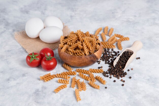 Eine Holzschale mit italienischen ungekochten trockenen Nudeln Fusilli mit Pfefferkörnern. Hochwertiges Foto