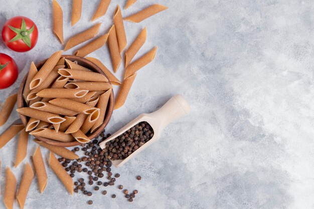 Eine Holzschale mit italienischer ungekochter trockener Pasta Penne Rigate mit Tomaten und Pfefferkörnern. Hochwertiges Foto