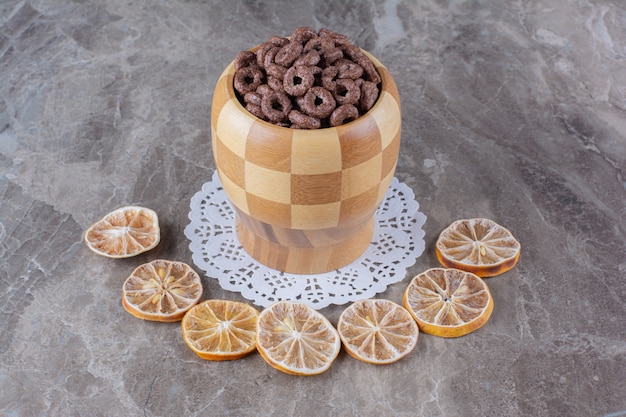 Eine Holzschale mit Schokoladen-Müsli-Ringen mit geschnittenen getrockneten Orangenfrüchten.