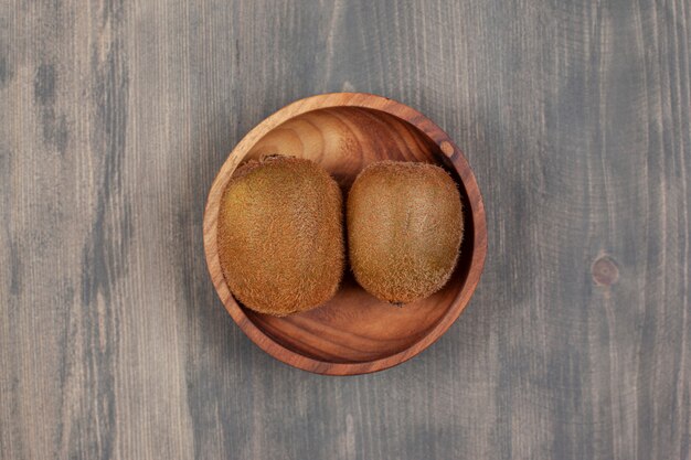 Eine Holzschale mit zwei frischen Kiwis auf einem Holztisch. Hochwertiges Foto