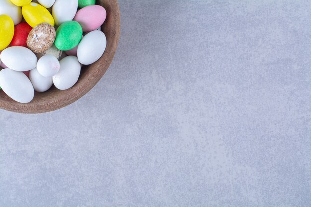 Eine Holzschale voller bunter Bohnenbonbons auf grauem Tisch.