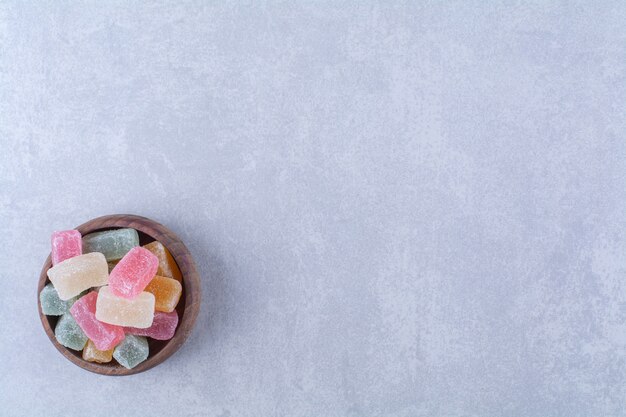 Eine Holzschale voller bunter Bohnenbonbons auf grauer Oberfläche