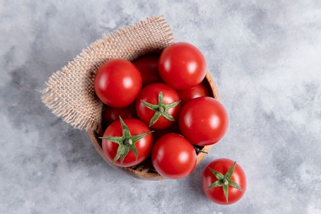 Eine Holzschale voller frischer saftiger roter Tomaten auf Steintisch. Hochwertiges Foto