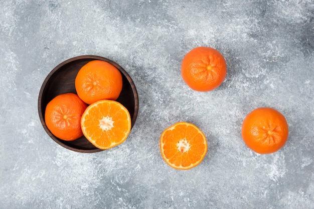 Eine Holzschale voller saftiger Orangenfrüchte auf Steintisch.