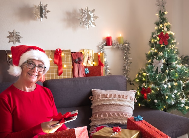 Eine hübsche ältere dame freut sich über das neue tablet, das gerade zu weihnachten geschenkt wurde. urlaubstag für ein rentner. sie lächelt, während sie auf dem sofa sitzt.