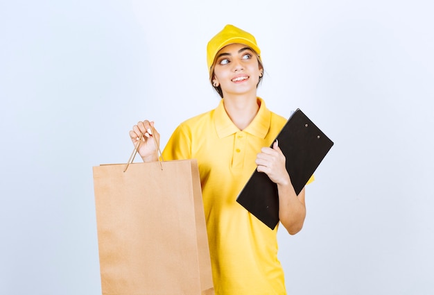 Eine hübsche Frau in der gelben Uniform, die braune leere Handwerkspapiertüte hält.