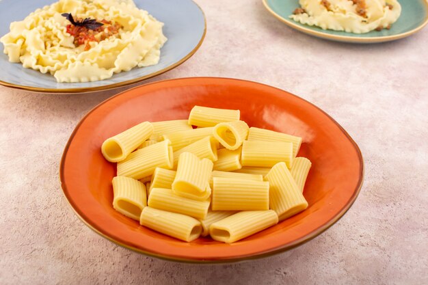 Eine italienische Pasta der Vorderansicht kochte lecker und gesalzen in runden orangefarbenen Teller auf rosa Schreibtisch