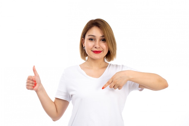 Eine junge Dame der Vorderansicht im weißen Hemd, das lächelnd zeigt, wie Zeichen auf dem Weiß zeigt