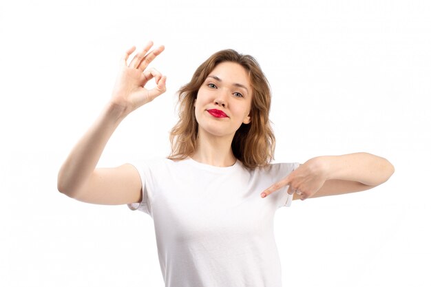 Eine junge Dame der Vorderansicht im weißen Hemd und in den schwarzen modernen Jeans, die lächelnd auf dem Weiß aufwerfen