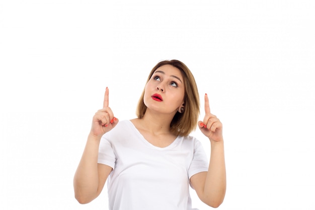 Eine junge Dame der Vorderansicht im weißen T-Shirt, das auf dem Weiß in den Himmel schauend aufwirft