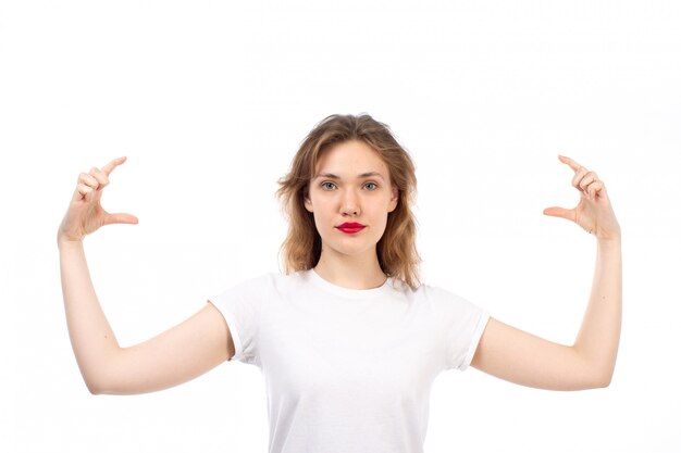 Eine junge Dame der Vorderansicht im weißen T-Shirt, das die Größe ihrer Finger auf dem Weiß zeigt