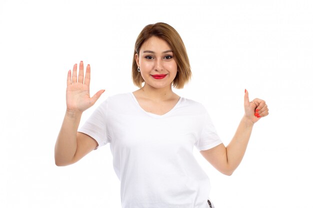Eine junge Dame der Vorderansicht im weißen T-Shirt, das lächelnd zeigt, wie Zeichen auf dem Weiß zeigt