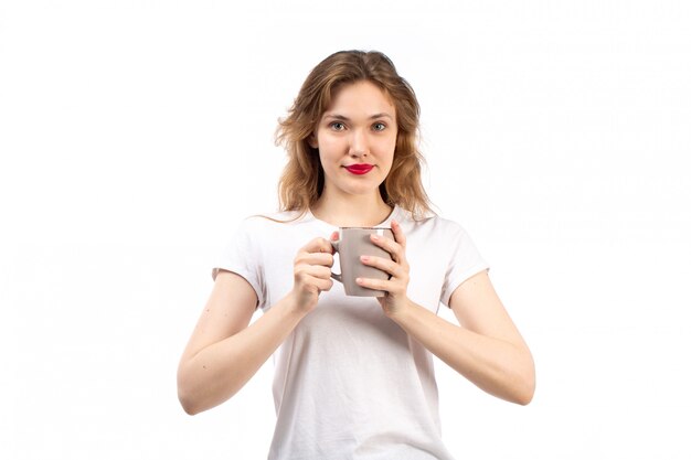 Eine junge Dame der Vorderansicht im weißen T-Shirt lächelnd halten Tasse auf dem Weiß