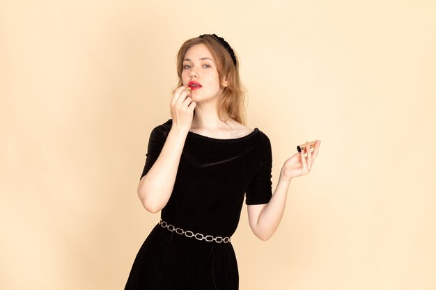 Eine junge Frau der Vorderansicht im schwarzen Kleid mit Kettengürtel, der Make-up auf Beige tut