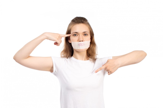 Eine junge Frau der Vorderansicht im weißen T-Shirt mit weißem Verband um ihren Mund auf dem Weiß